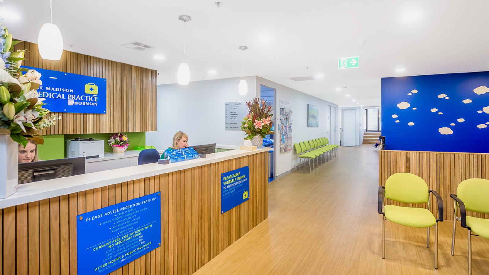 Modern medical practice reception area with wood panelling, green chairs and blue branding at Madison Medical