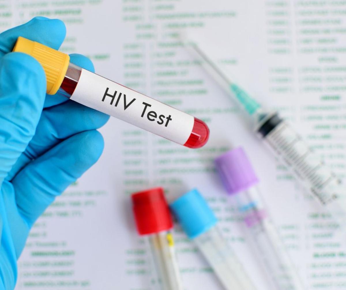 Healthcare professional in blue gloves holding HIV test tube with red blood sample