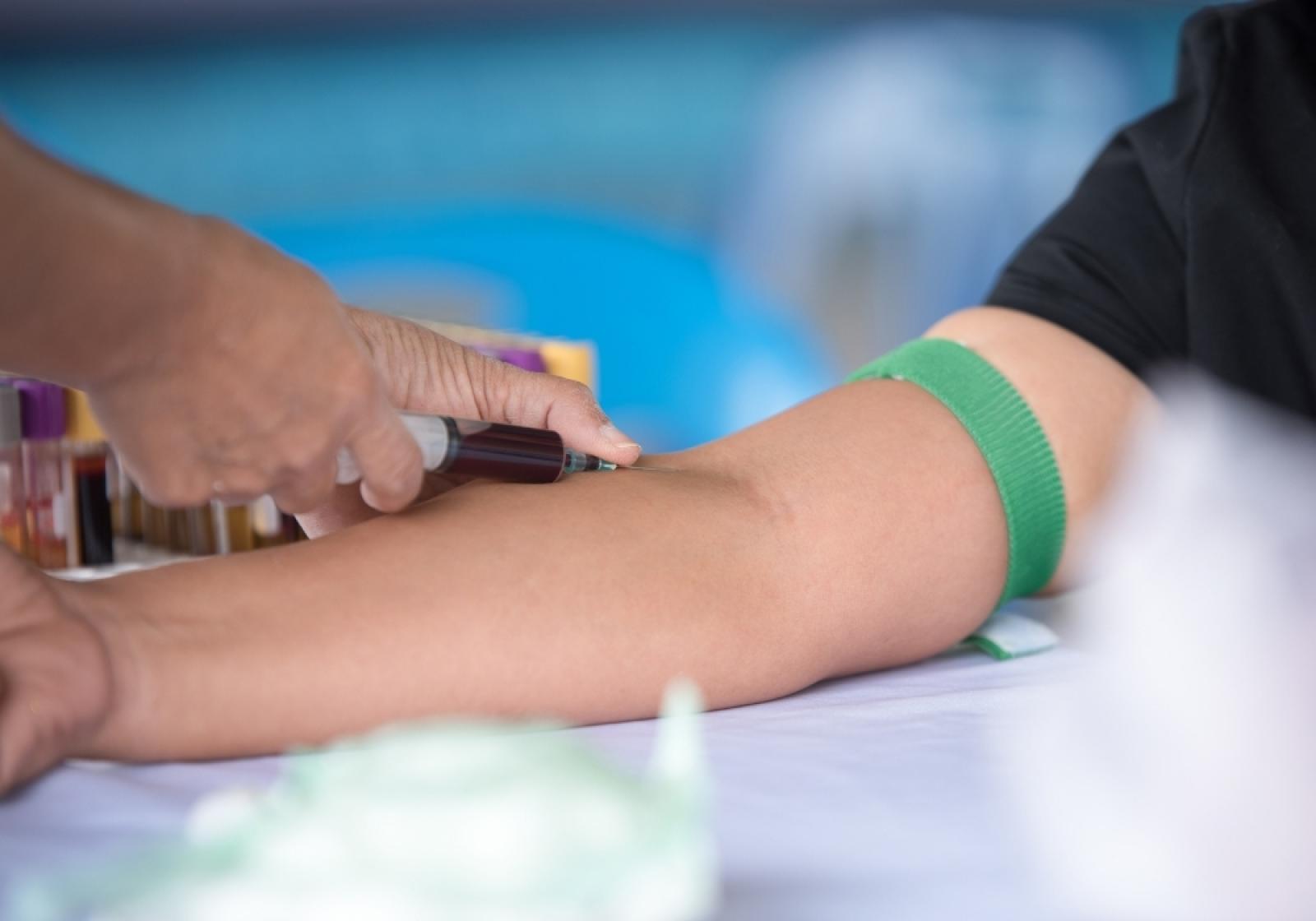 Healthcare professional performing a blood test on a patient's arm with a green identification band
