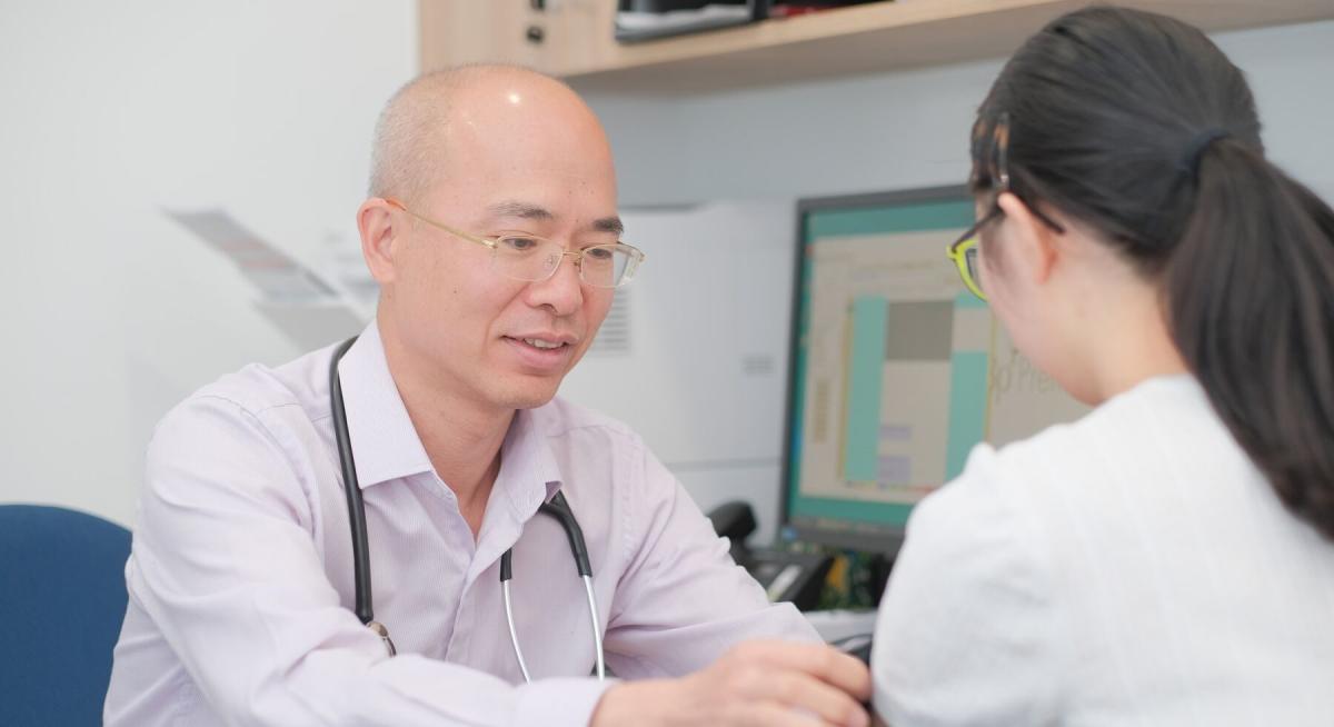 Male doctor in glasses and stethoscope consulting with female patient in clinical examination room