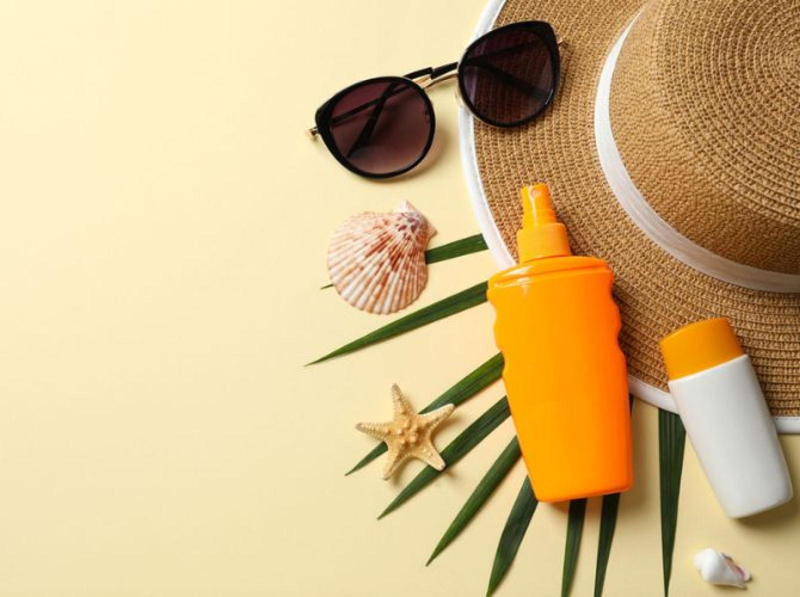 Sunscreen bottles and sunglasses with beach accessories on cream background