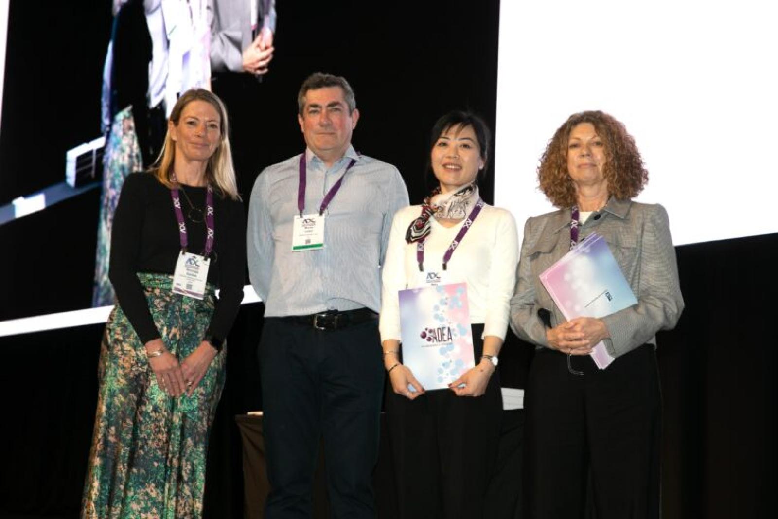 Four healthcare professionals wearing conference badges standing together on stage at a medical conference event